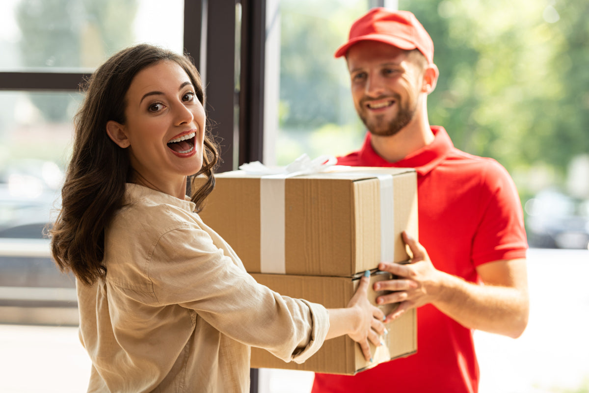 Woman receiving a package from a delivery person in a red shirt.