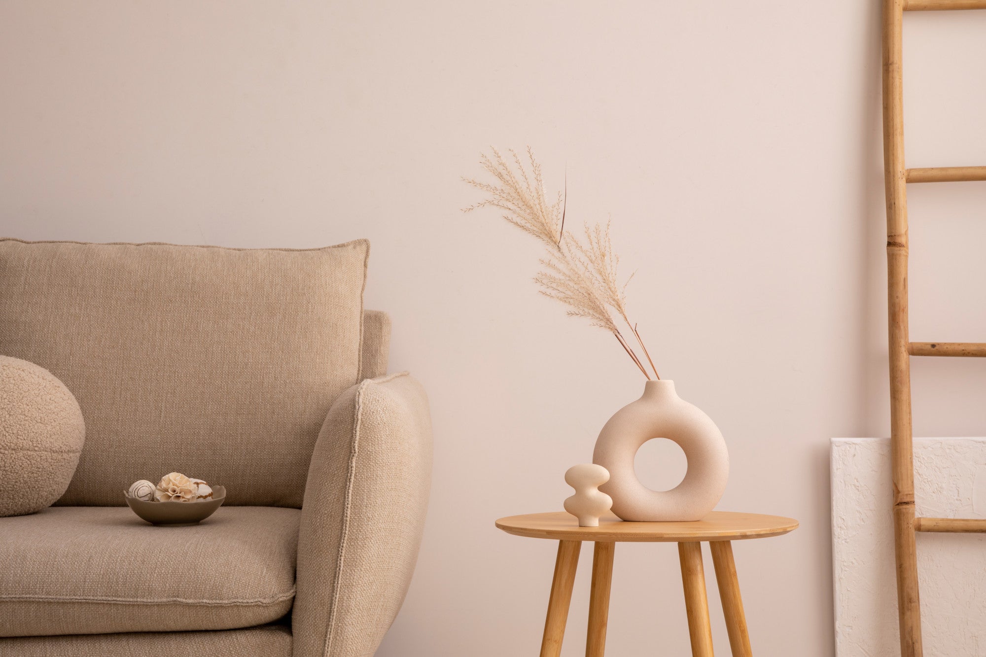 Beige sofa with a small table and decorative items against a light pink wall.